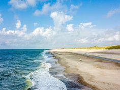 people are walking on the beach by the water's edge as waves come in