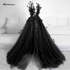 two black dresses with flowers on them are sitting on a white rug in front of a couch