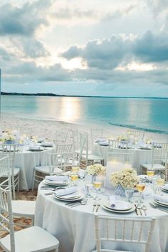 tables set up on the beach with white linens and silverware for an elegant dinner