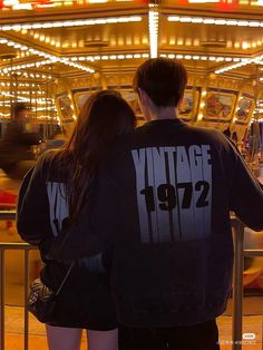 a man and woman standing in front of a carousel at an amusement park with their back to the camera