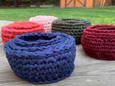 four crocheted baskets sitting on top of a wooden table in front of grass