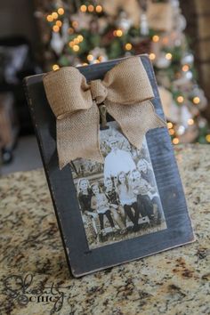 an old fashioned photo frame with a bow on it sitting in front of a christmas tree