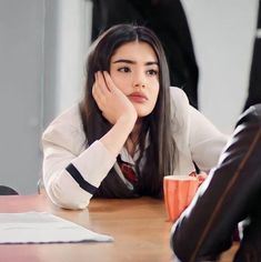 a woman is sitting at a table with her hand on her head and looking away from the camera