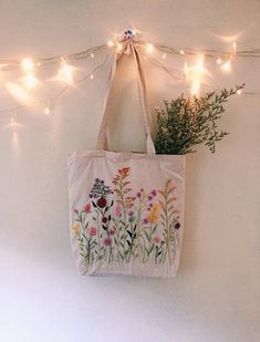 a tote bag hanging on a wall with lights in the background and flowers painted on it