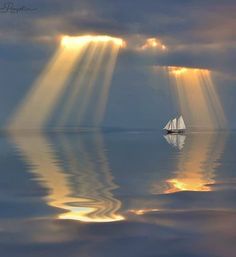 a sailboat floating on top of a body of water under cloudy skies with sunbeams