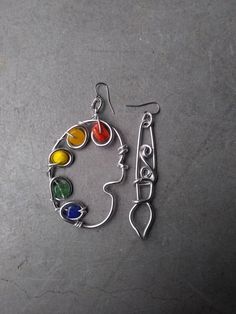 a pair of earrings with different colored stones in the shape of a woman's face