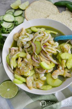 a white bowl filled with shrimp and cucumbers next to sliced bread on a table