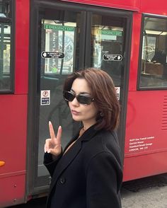 a woman standing in front of a red bus giving the peace sign with her hand