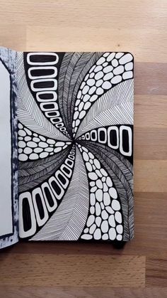 an open notebook with black and white designs on the cover, sitting on a wooden surface