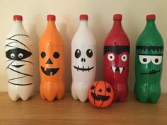 four plastic bottles with faces painted on them sitting next to an orange and green pumpkin