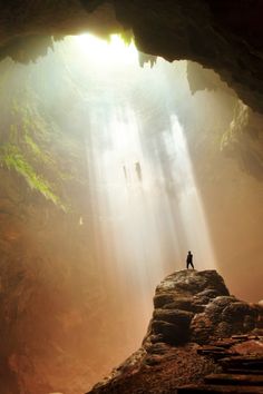 a person standing in the middle of a cave with light coming from it's ceiling