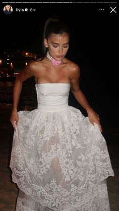 a woman in a white dress is standing on the beach with her hands behind her back