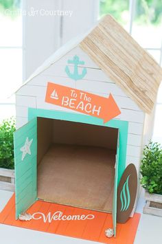 an open dog house made out of cardboard with the words welcome to the beach on it