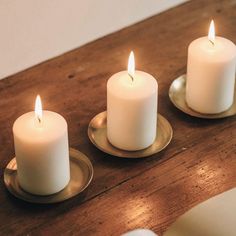 three white candles sitting on top of a wooden table