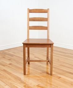 a wooden chair sitting on top of a hard wood floor next to a white wall