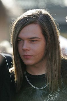 a young man with long hair wearing a black t - shirt and silver chain necklace