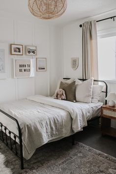 a bedroom with white walls and pictures on the wall above the bed, along with a teddy bear