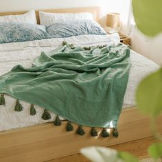 an unmade bed with green tassels on it