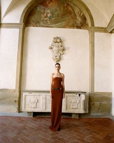 a woman in a red dress standing next to a wall with a painting on it