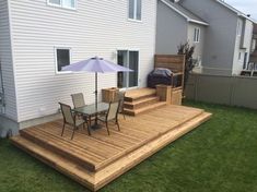 a deck with chairs and an umbrella next to a house on the grass in front of it