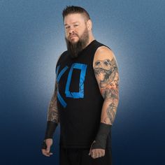 a man with a beard and tattoos standing in front of a blue background wearing a black tank top