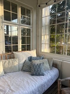 a white couch with pillows on it in front of two windows and a wooden bench