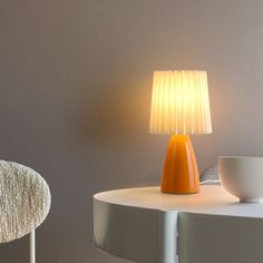 an orange lamp sitting on top of a table next to a white bowl and chair