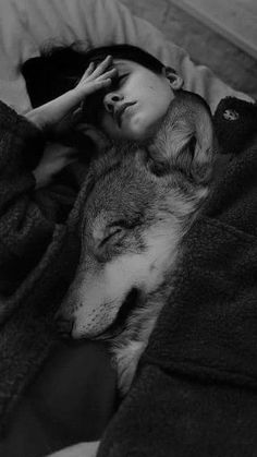 a black and white photo of a woman laying in bed next to a sleeping wolf