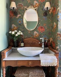 a bathroom sink sitting under a mirror next to a wooden vanity with flowers on it