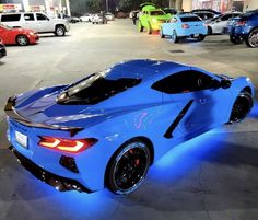 a blue sports car parked in a parking lot at night with other cars behind it