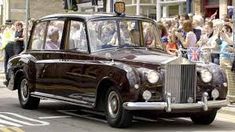 an old fashioned car driving down the street in front of a large group of people