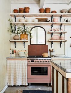 a pink stove top oven sitting inside of a kitchen next to a wooden shelf filled with pots and pans