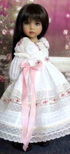 a doll with long black hair wearing a white dress and pink ribbon around the waist