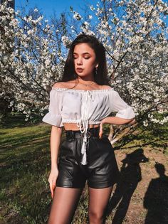 a woman standing in front of a tree wearing black leather shorts and off the shoulder top