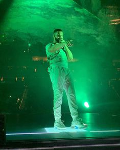 a man standing on top of a stage in front of green lights with his hands up