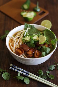 a white bowl filled with noodles, meat and veggies next to chopsticks