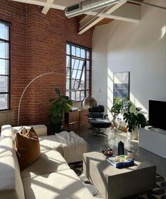 a living room filled with lots of furniture next to large windows on top of a brick wall