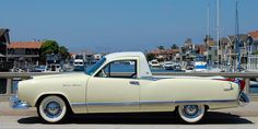 an old white car parked in front of a marina