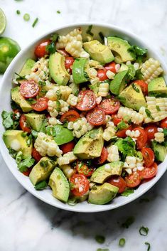 a white bowl filled with corn, avocado and tomato salad on top of a marble counter