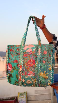 a person holding up a large green bag with flowers on the front and bottom part