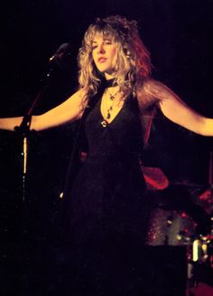 a woman standing in front of a microphone on stage with her arms spread out to the side