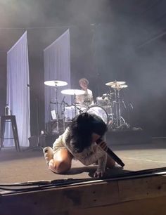 a person on the ground in front of a stage with drummers and drums behind them