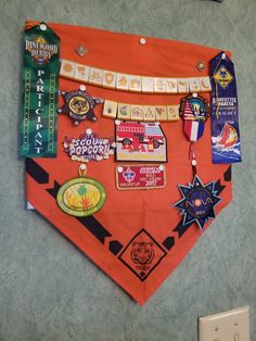 an orange bandana with various badges and pins attached to it on the wall in front of a light switch