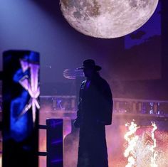 a man in a long coat and hat standing next to a stage with bright lights