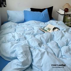 an unmade bed with blue sheets and pillows on top of it, next to a night stand