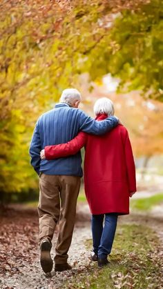 an older couple walking down a path in the fall with their arms around each other