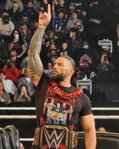 a man standing in front of a crowd with his hand up and wearing a wrestling belt