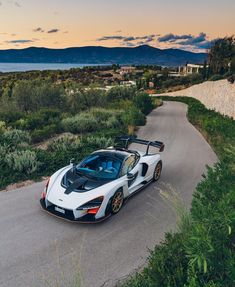 a white and black sports car driving down a road next to the ocean with mountains in the background