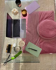 a laptop computer sitting on top of a glass table next to a pink pillow and other items