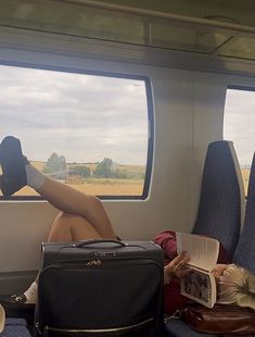 a woman laying on top of a seat next to a window with an open book